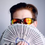 salary loan man in black framed sunglasses holding fan of white and gray striped cards