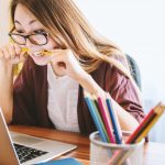 mental health woman biting pencil while sitting on chair in front of computer during daytime