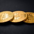 three gold-colored bitcoins on black surface