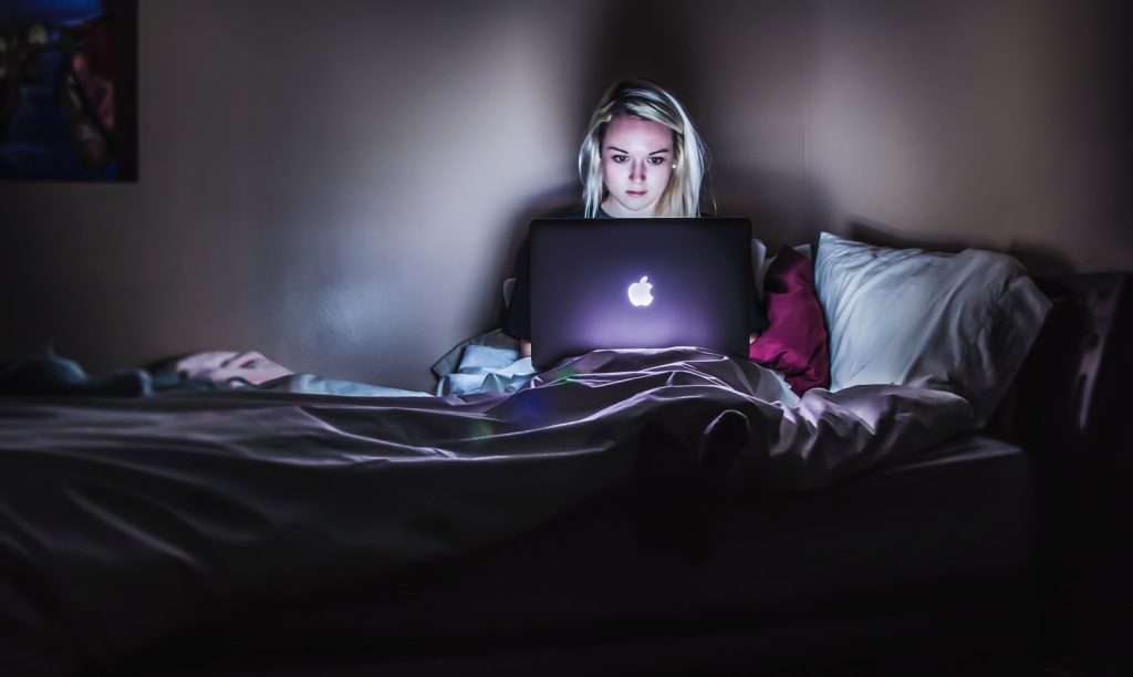 online fraud woman sitting on bed with MacBook on lap