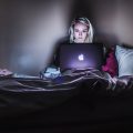 online fraud woman sitting on bed with MacBook on lap