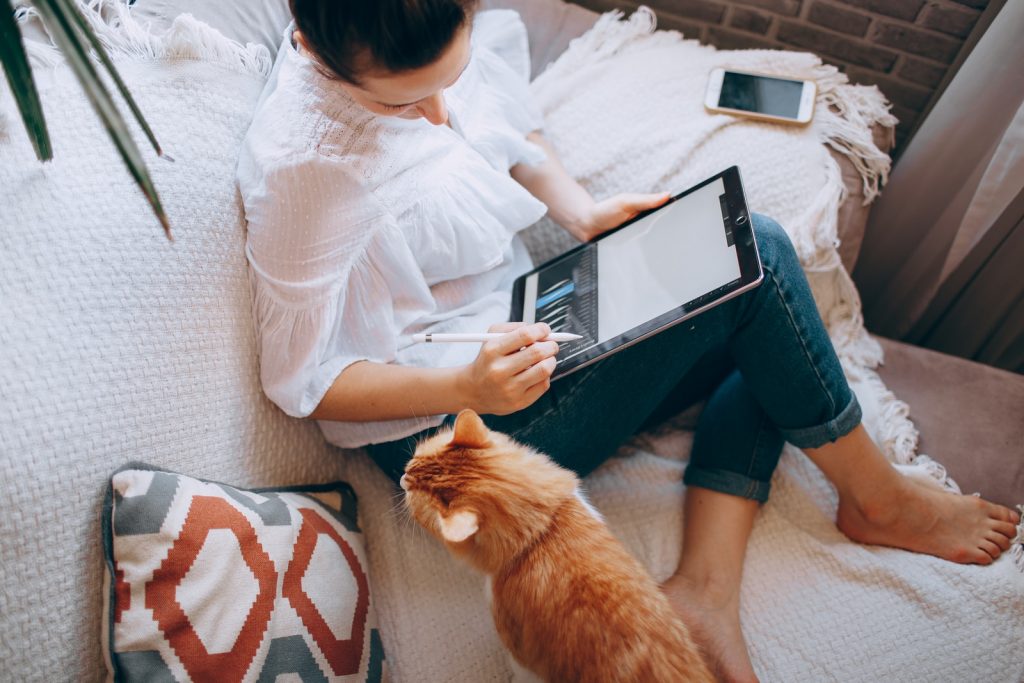 Working from Home woman in white long sleeve shirt and blue denim shorts sitting on bed using tablet computer