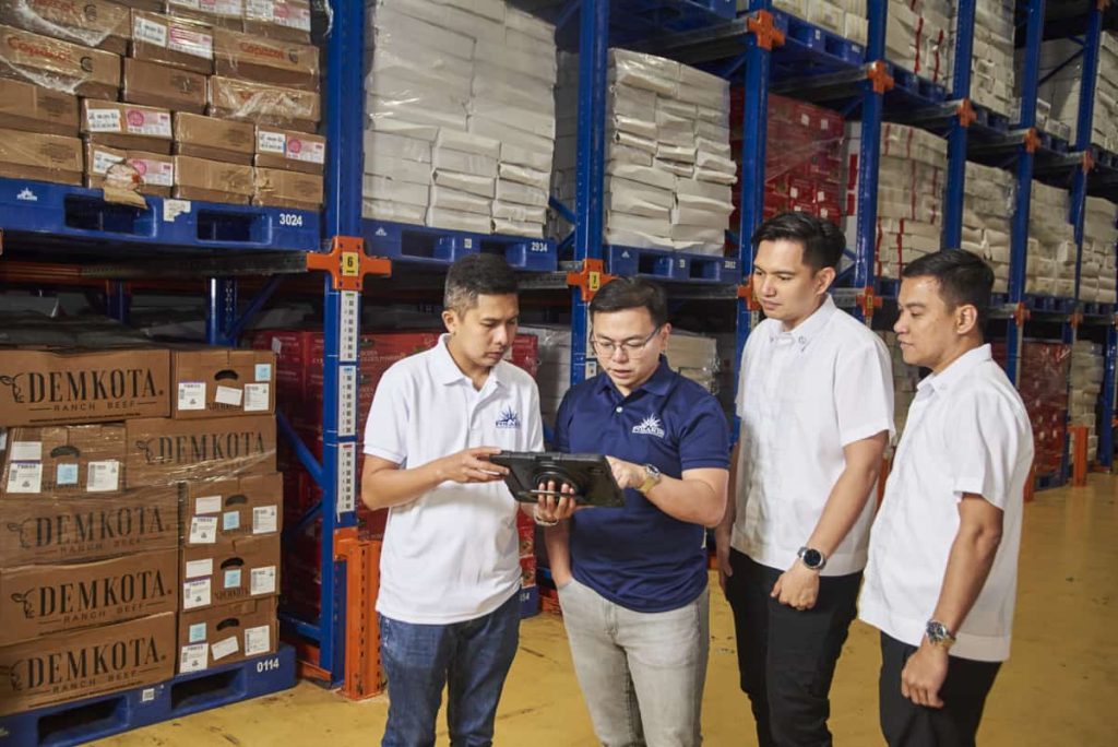 a group of men standing at a warehouse looking at the tablet