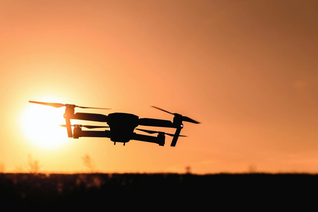 Urban Tech- A drone in silhouette against a vibrant orange sunset sky, showcasing modern technology and aerial photography.