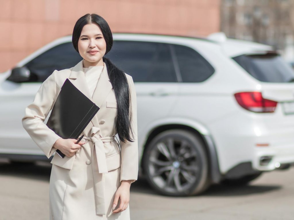 Car Insurance Quotes- Smiling professional woman standing confidently by a luxury car, embodying success.