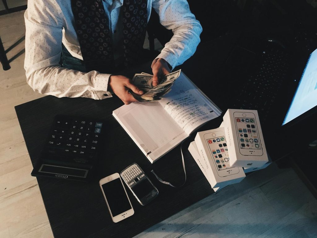 Psychological Pricing- Businessman organizing finances with tech devices and cash on desk.