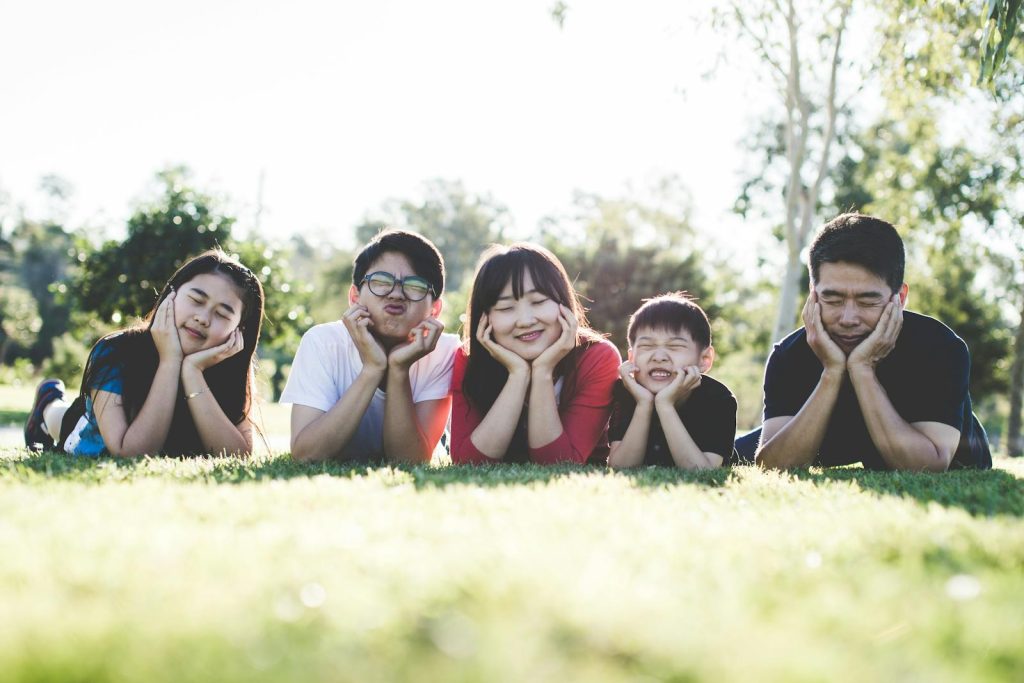 baby bonus- Asian family posing happily on the grass in a sunny park, showcasing love and togetherness.
