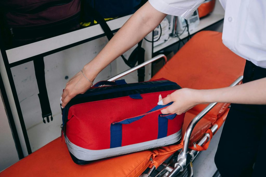 Medicine Kits- A healthcare worker reaches for a red medical bag on a stretcher indoors.
