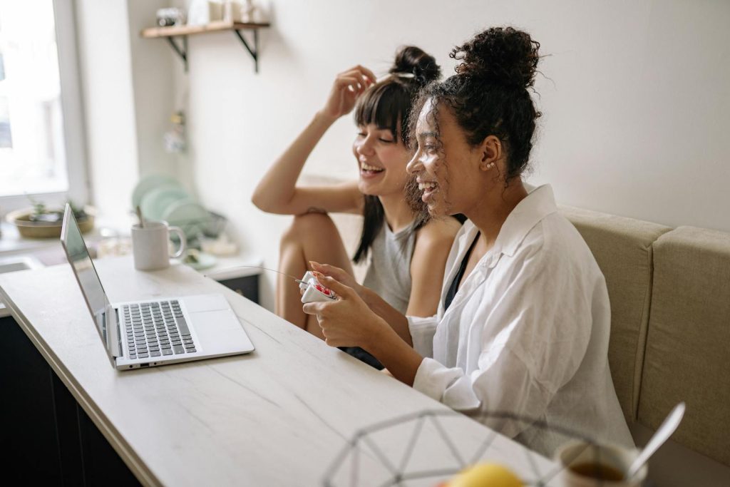 Play-to-Earn Games- Happy women playing video games on a laptop in a cozy indoor setting.