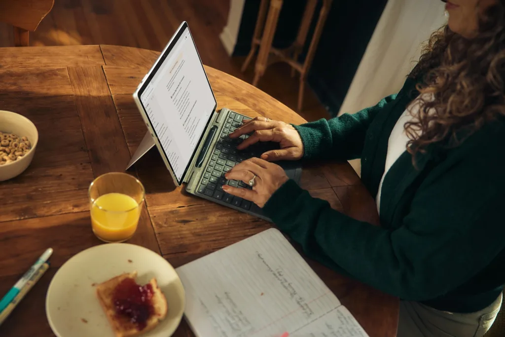 From Apps to Websites: How Age Verification Ensures Responsible Access 1 Woman typing on laptop at wooden table with breakfast.