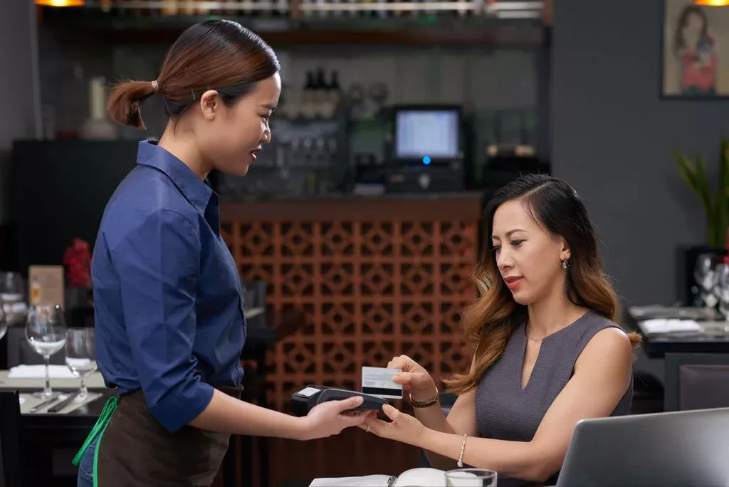 A customer paying her bill with a credit card using a handheld payment terminal held by a waitress in a restaurant.